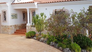 Un edificio blanco con base de piedra, techo de tejas y acceso pavimentado.