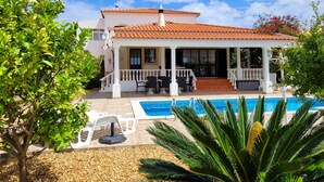 Una casa de dos pisos con techo de tejas, piscina y un patio cubierto.