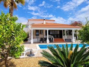 A two-story house with a tiled roof, a swimming pool, and a covered patio area.