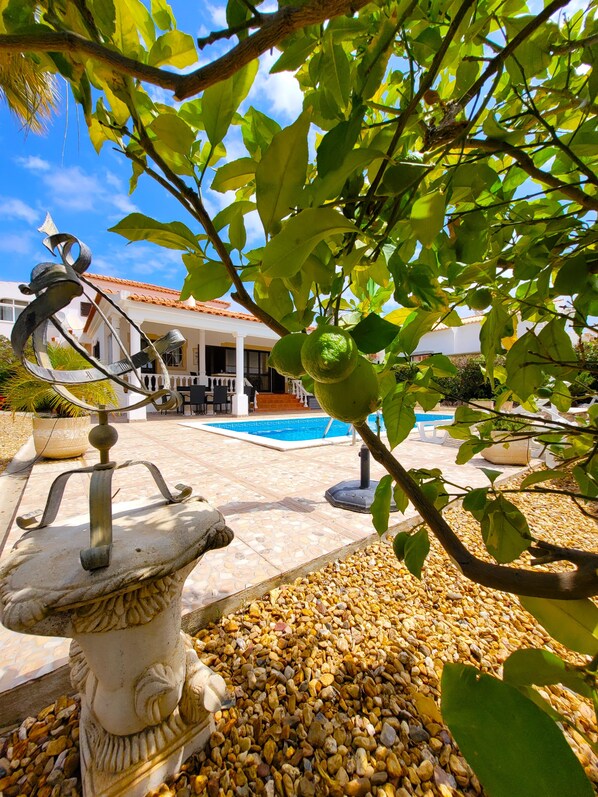 A pool area with a stone sculpture, pebbles, and a view of a building with a tiled roof.