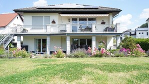 A two-story house with a balcony, a staircase, and a garden with various flowers.