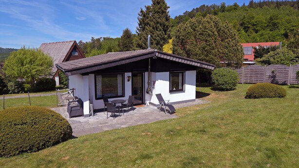 Een klein, modern huis met terras, barbecueplaats en uitzicht op het omliggende bos.