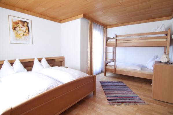 A bedroom with a single bed, a bunk bed, wooden flooring, a painting on the wall, and a striped rug. - 4 to 12 people, ski vacation, hiking vacation, cultural vacation, quiet dreamlike location (Schlitters)