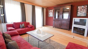 A living room with a red sofa, a coffee table, a wooden cabinet, and a flat-screen TV. - 4 to 12 people, ski vacation, hiking vacation, cultural vacation, quiet dreamlike location (Schlitters)
