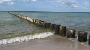 Une plage avec une jetée en bois qui s’avance dans la mer, et les vagues qui viennent doucement lécher le rivage.