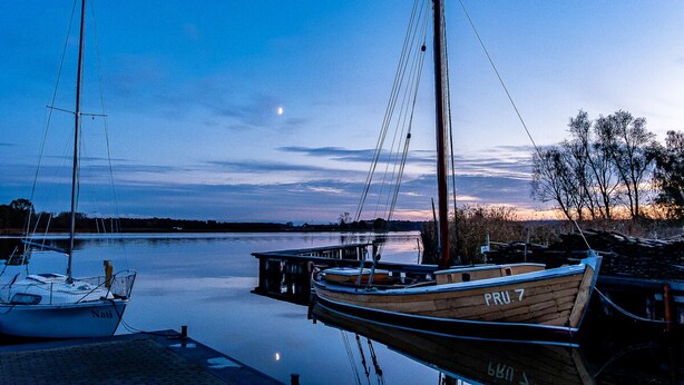 Un port de plaisance paisible, avec des bateaux amarrés, un ciel dégagé et une lune bien visible.