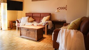 A cozy living room with a brown leather sofa, a wooden coffee table, and a television mounted on the wall. - Cozy vacation apartment in the countryside - ideal for switching off & relaxing (Niederbobritzsch)