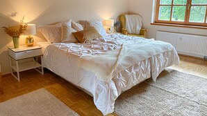 A bedroom with a bed, bedside tables, a chair, a window, and a radiator. - Cozy vacation apartment in the countryside - ideal for switching off & relaxing (Niederbobritzsch)