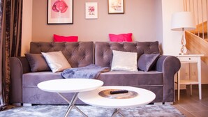 Ein modernes Wohnzimmer mit einem grauen Sofa, zwei weißen Beistelltischen und einer Treppe im Hintergrund.