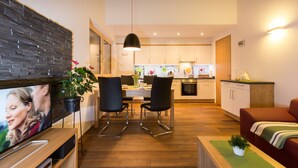 Un salon moderne avec un téléviseur à écran plat, un coin repas avec des chaises, une cuisine en arrière-plan et un canapé rouge.