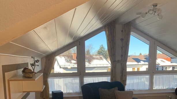 A cozy loft apartment with a dark-colored sofa, a wooden floor, and a large window offering a view of the neighborhood.