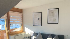 A bedroom with a large bed, star-patterned bedding, two framed artworks on the wall, and a window with blinds.