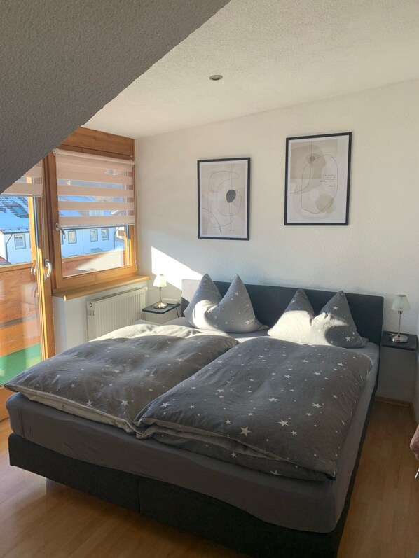 Une chambre avec un grand lit, une literie ornée de motifs étoilés, deux œuvres d’art encadrées accrochées au mur et une fenêtre avec des stores.