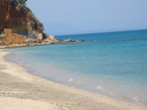 Una playa con agua cristalina, orilla arenosa y acantilados rocosos.