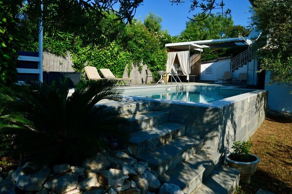 Piscina con escalones de acceso, rodeada de un muro de piedra y plantas en macetas.