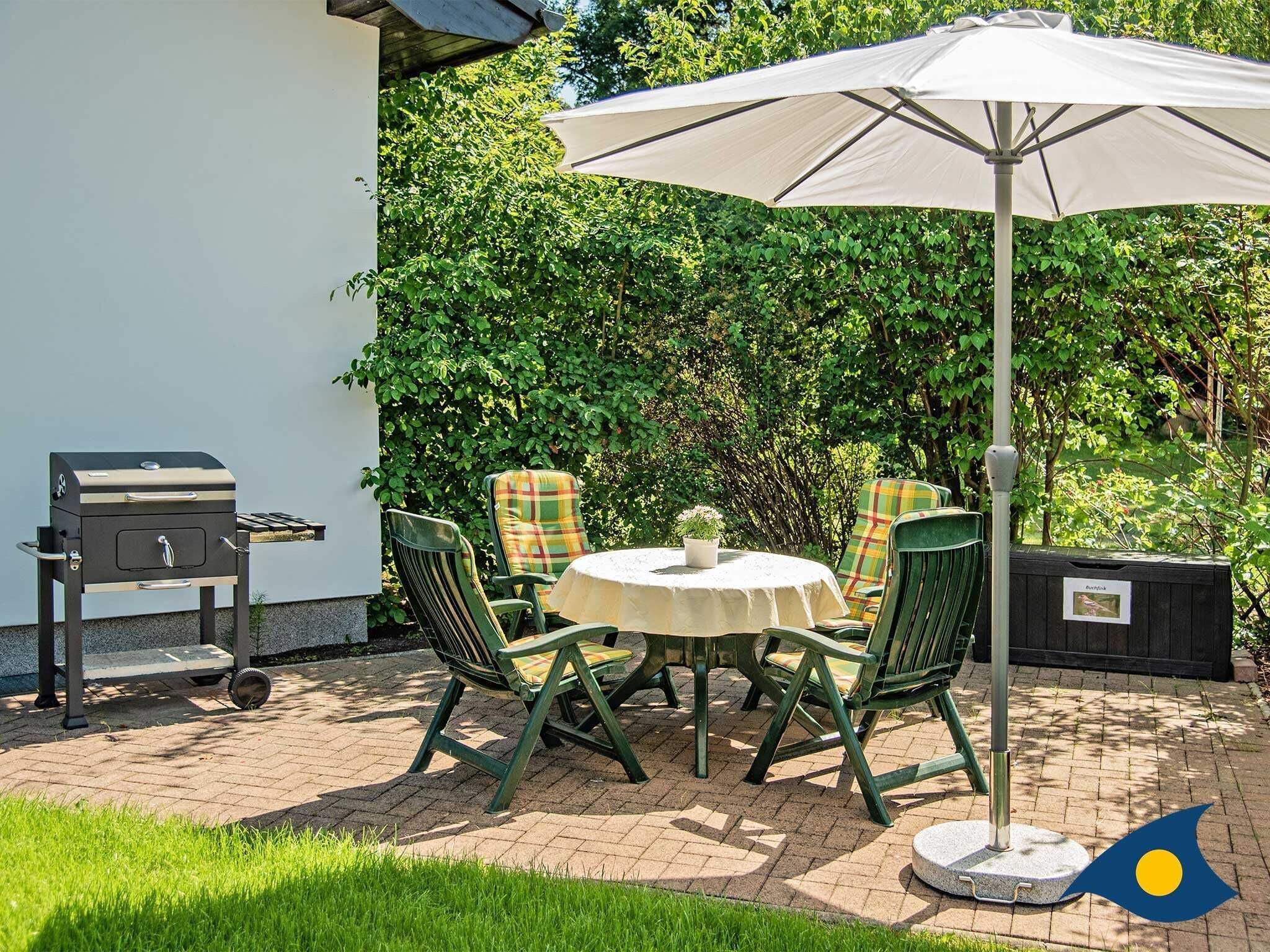 An outdoor patio with a round table, four chairs, a grill, and an umbrella.