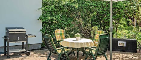 An outdoor patio with a round table, four chairs, a grill, and an umbrella.