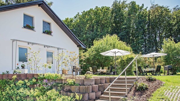Ein weißes Haus mit Garten, Außenbereich zum Sitzen und einer Treppe, die zu einer Terrasse führt.