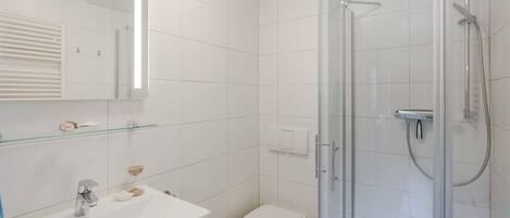 Un baño moderno con cabina de ducha de vidrio, un lavabo blanco con posavaso de vidrio y un inodoro.