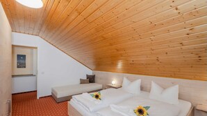 Ein Schlafzimmer mit schrägem Dach, einem Bett mit weißen Leinen und Sonnenblumen, einem kleinen Sofa, einem Nachttisch mit Lampe und einem Gemälde an der Wand.