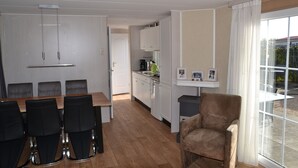 Ein modernes Zimmer mit Esstisch und Stühlen, einer Küchenzeile und einem großen Fenster mit Vorhängen.