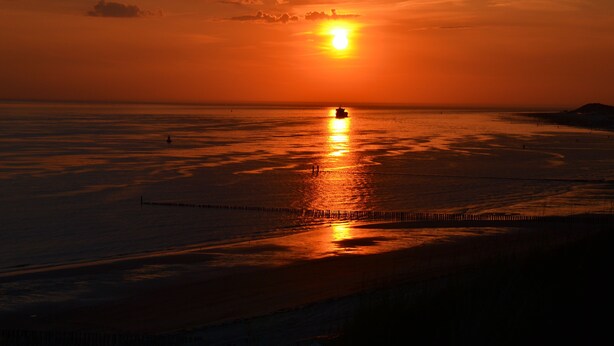 Ein Sonnenuntergang über einem ruhigen Meer mit einem Schiff in der Ferne.