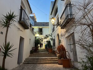 A narrow street with buildings on either side, a staircase leading to a second floor, and potted plants along the path. - Lovely holiday home with a sun terrace, pool and own garden (Altea)