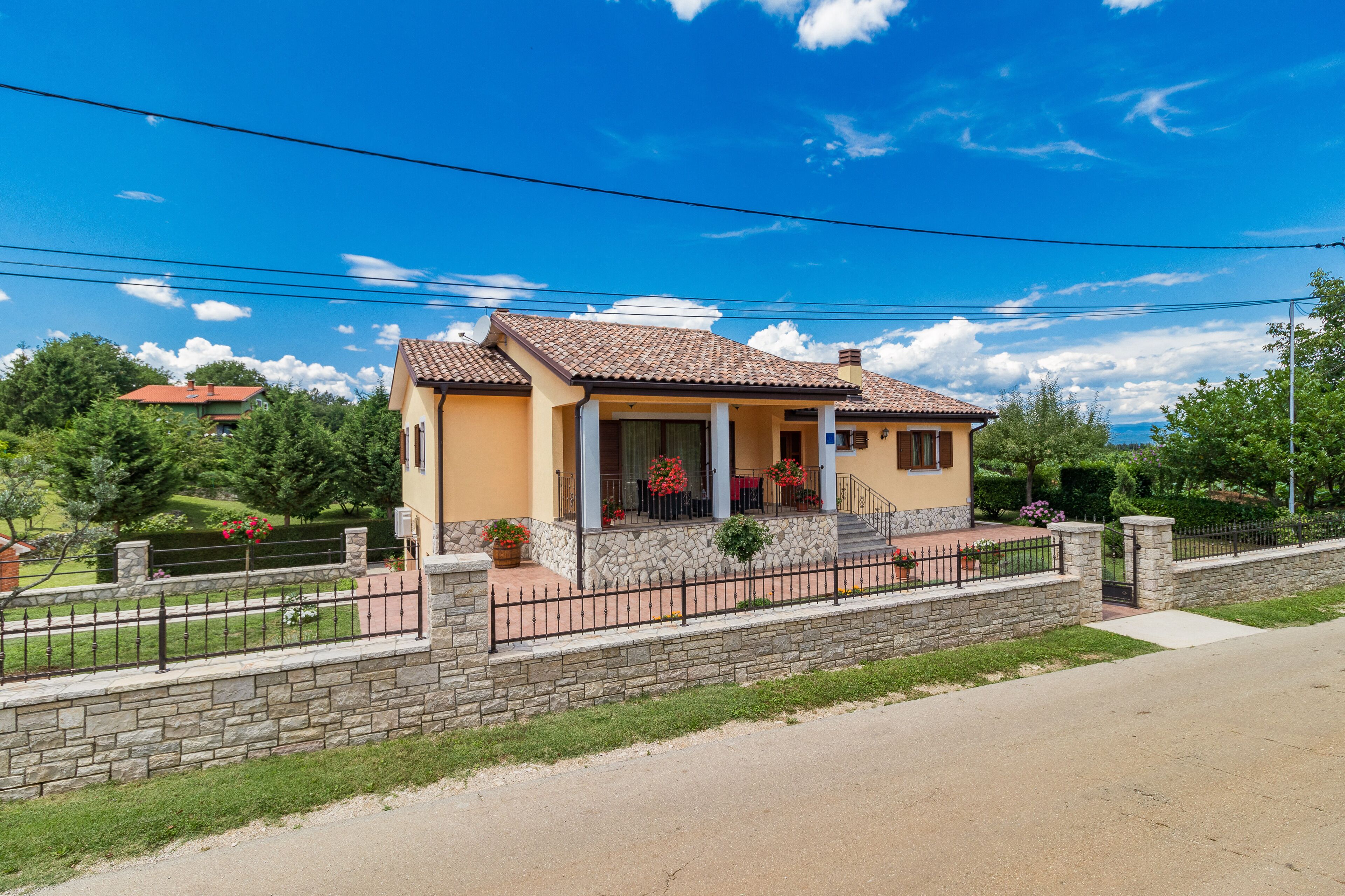 Una casa de dos pisos con un muro de piedra y una cerca de metal al frente.