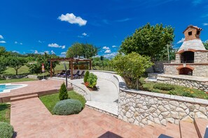A patio area with a stone wall, a pergola, and a stone oven.