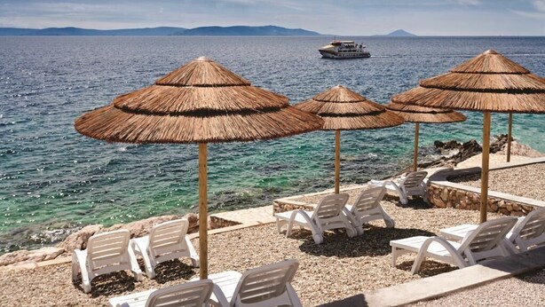 A beach with thatched umbrellas and white lounge chairs, a boat in the background, and clear blue water. - New luxurious and modern Villa, 5 minutes from the nearest beach (Krsan)