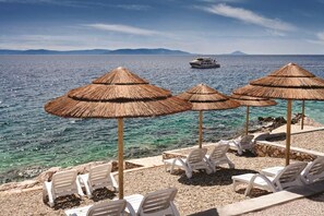 A beach with thatched umbrellas and white lounge chairs, a boat in the background, and clear blue water.