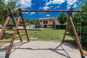 A wooden swing set in a backyard with a house and pool in the background.