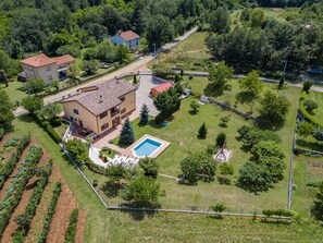 An aerial view of a residential property with a large house, a swimming pool, and a well-maintained garden.