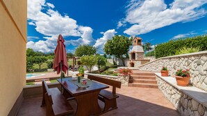 An outdoor patio with a wooden table and benches, a stone wall, and a view of a pool and garden. - New luxurious and modern Villa, 5 minutes from the nearest beach (Krsan)