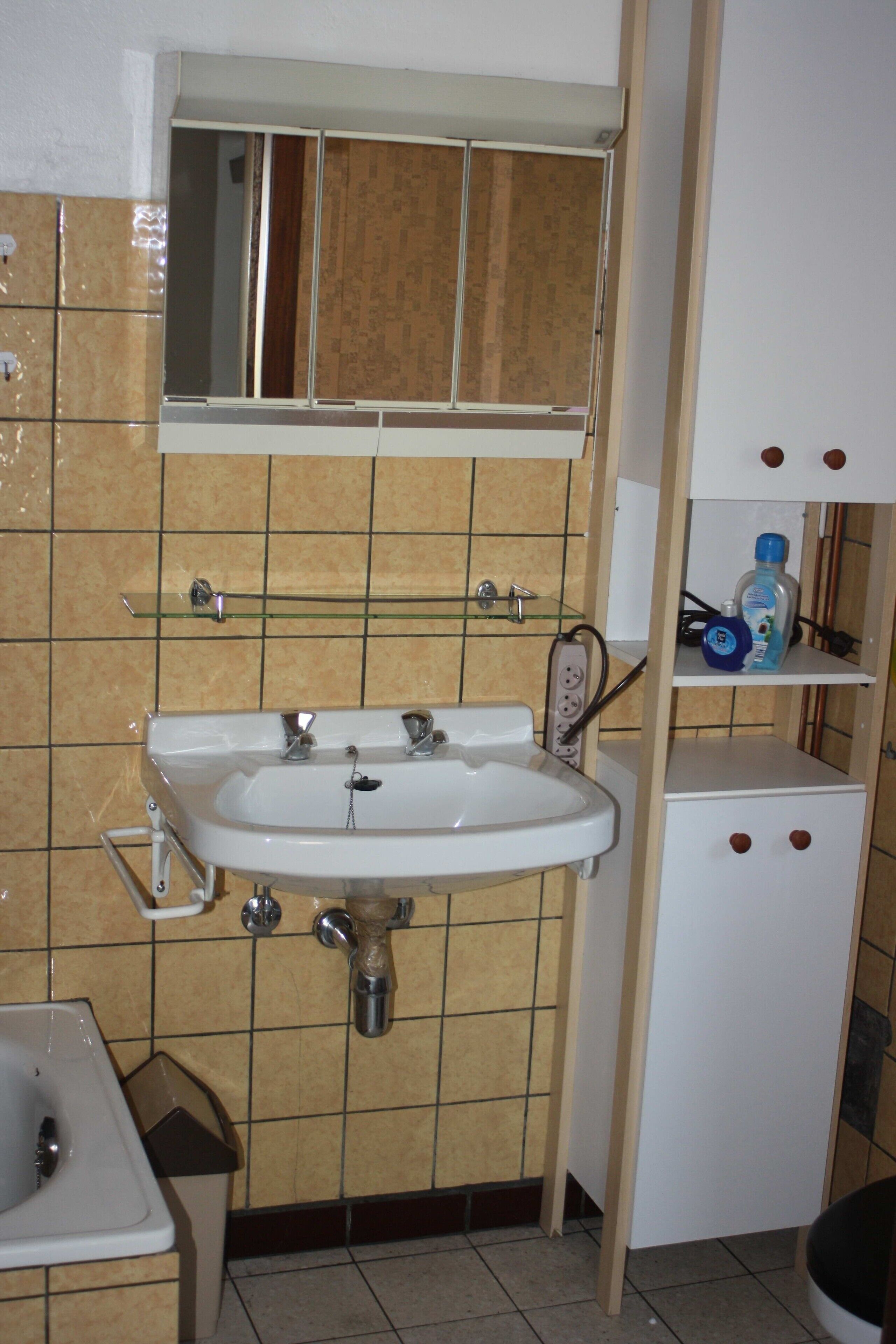 A bathroom with a white sink, a mirror above it, and a tiled wall.