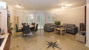 A modern living room with a dining area, a grey sofa, and a coffee table. - Vacation home-Fehmarn (Fehmarn)