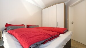 A bedroom with a bed, white walls, and a wardrobe. - Vacation home-Fehmarn (Fehmarn)