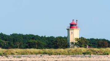 Un faro en una playa arenosa con vegetación densa al fondo.