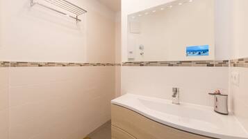 Une salle de bain avec un lavabo blanc, un miroir et un espace douche.
