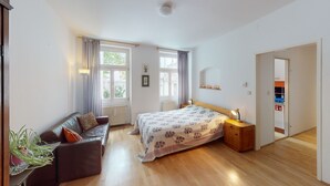 Quarto com cama, mesa de cabeceira de madeira, sofá de couro e planta em vaso.