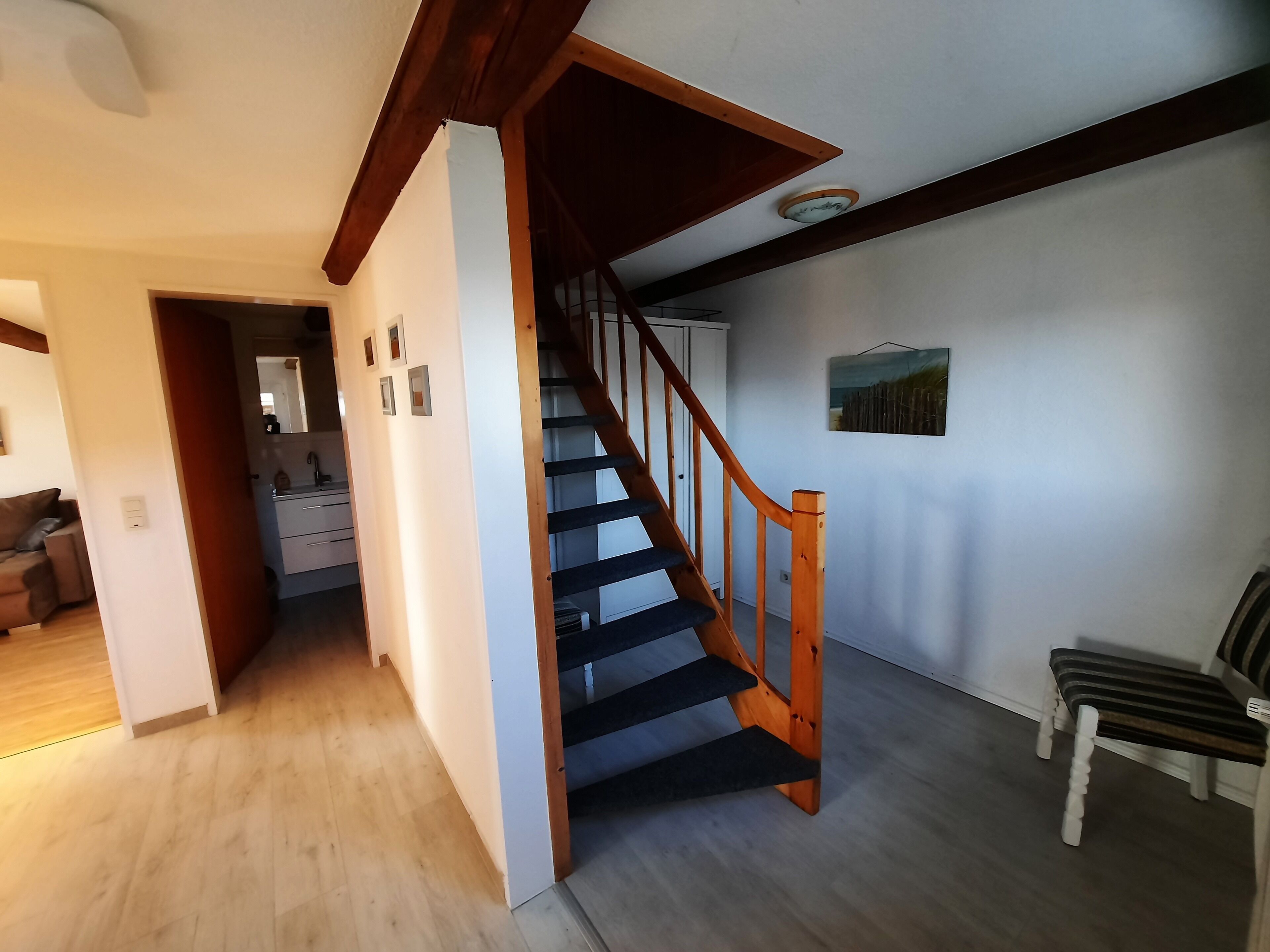 A staircase with wooden railings leading to a second floor, a bench, and a painting on the wall.