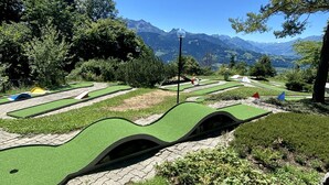 En minigolfbane med grønt kunstgræs, en lygtepæl og et bjergrigt baggrundsmotiv.