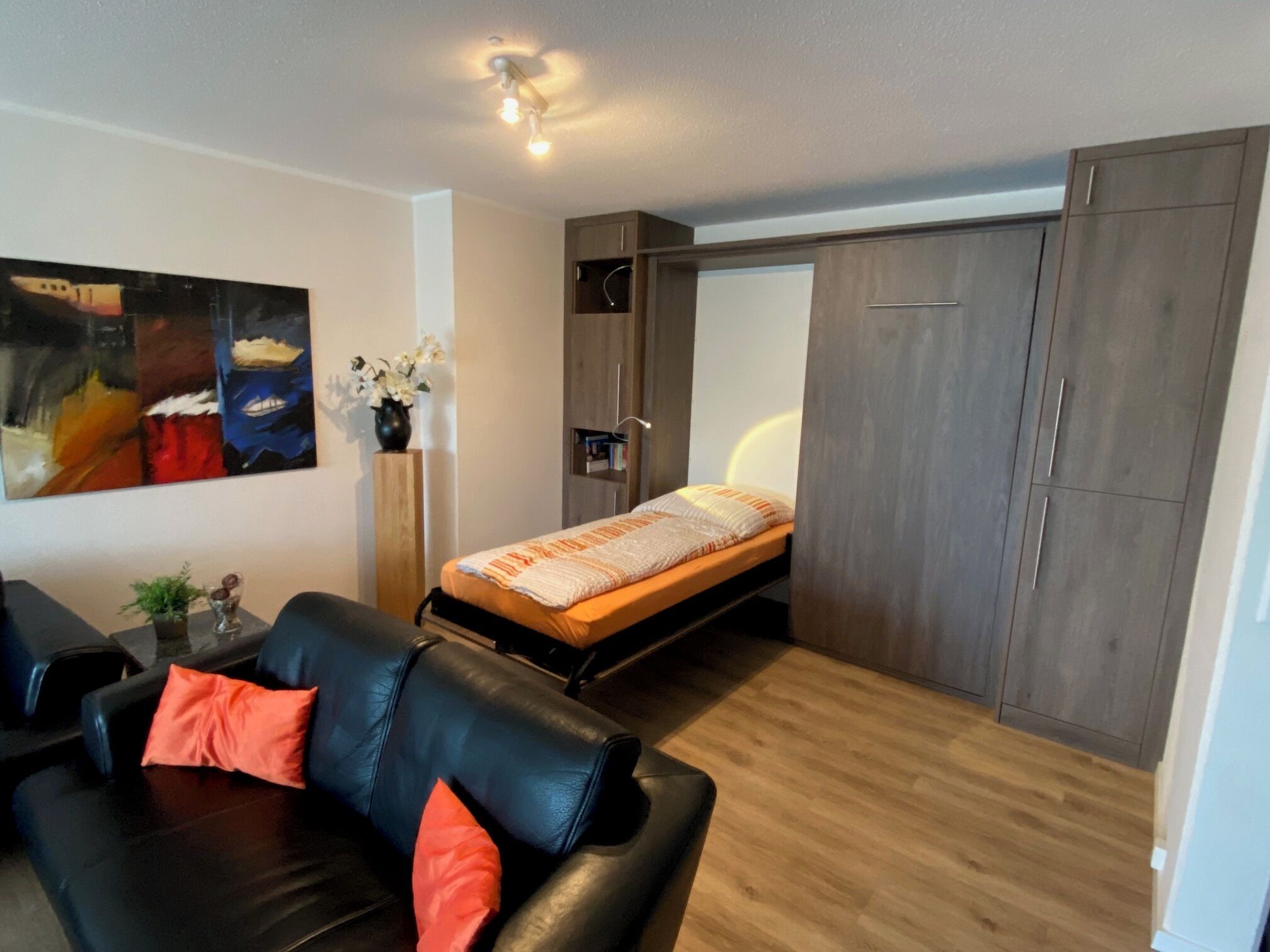 Een kleine kamer met een bed, een slaapbank, een bureau en een kledingkast.
