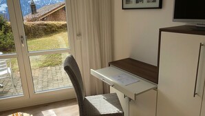 Et værelse med et stort vindue, en fletstol, et skrivebord og et skab.