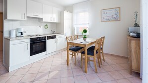 Une cuisine moderne avec des meubles blancs, une table à manger avec des chaises et une petite plante en pot.