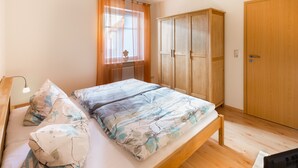 Une chambre à coucher avec un lit, une armoire en bois, un bureau avec une lampe et une fenêtre ornée de rideaux légers.