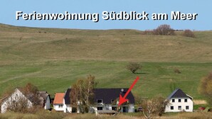 A lakeside property with a house highlighted by a red arrow, surrounded by a grassy landscape and a stone wall. - Exclusive apartment with sea views, south-facing terrace, garden u. parking spot (Groß Zicker)