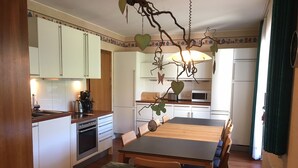 A modern kitchen with white cabinets, a central island, and a dining area with a wooden table and chairs. - Panorama-FeWo**** BEI WINTERBERG, 2 -10 pers., box-spring beds, WIFI / WLAN  (Schmallenberg)