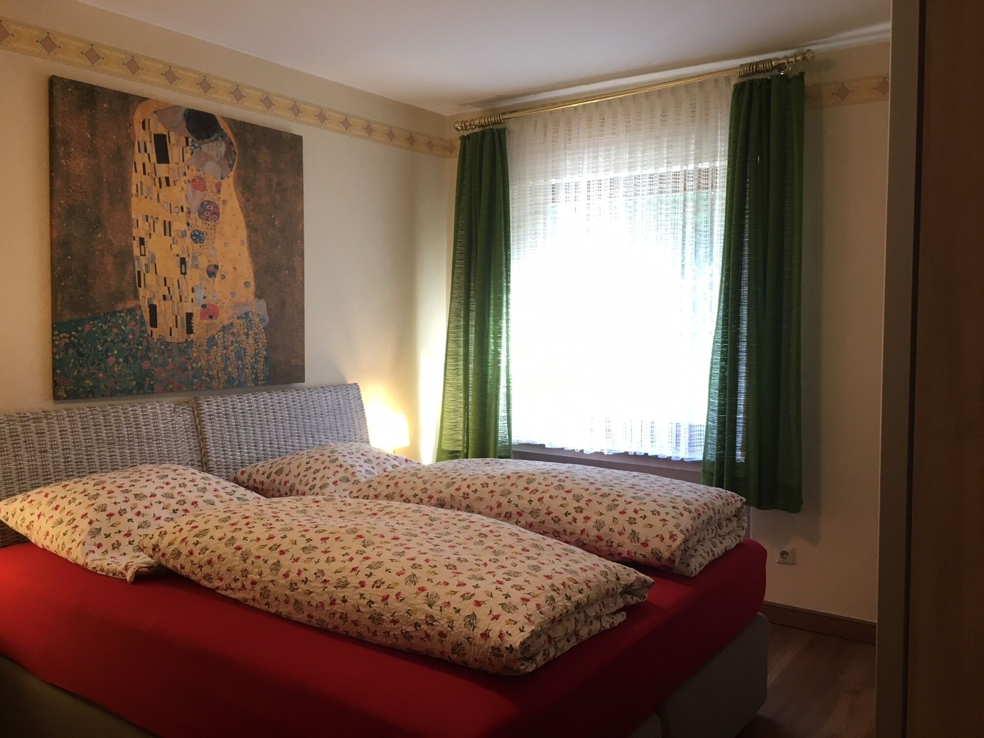 A bedroom with a bed, a painting, and a window with curtains.