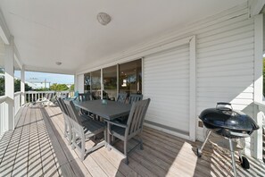 A covered outdoor patio with a dining table and chairs, a barbecue grill, and a view of the house in the background.